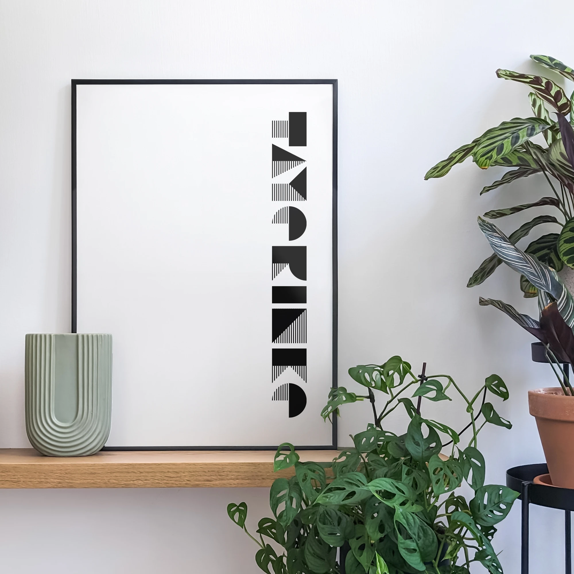 פוסטר גרפי של המילה Tayerinke ביידיש, מעוצב בסגנון באוהאוס, נשען על מדף עץ ולצידו פריטי עיצוב ועציצים