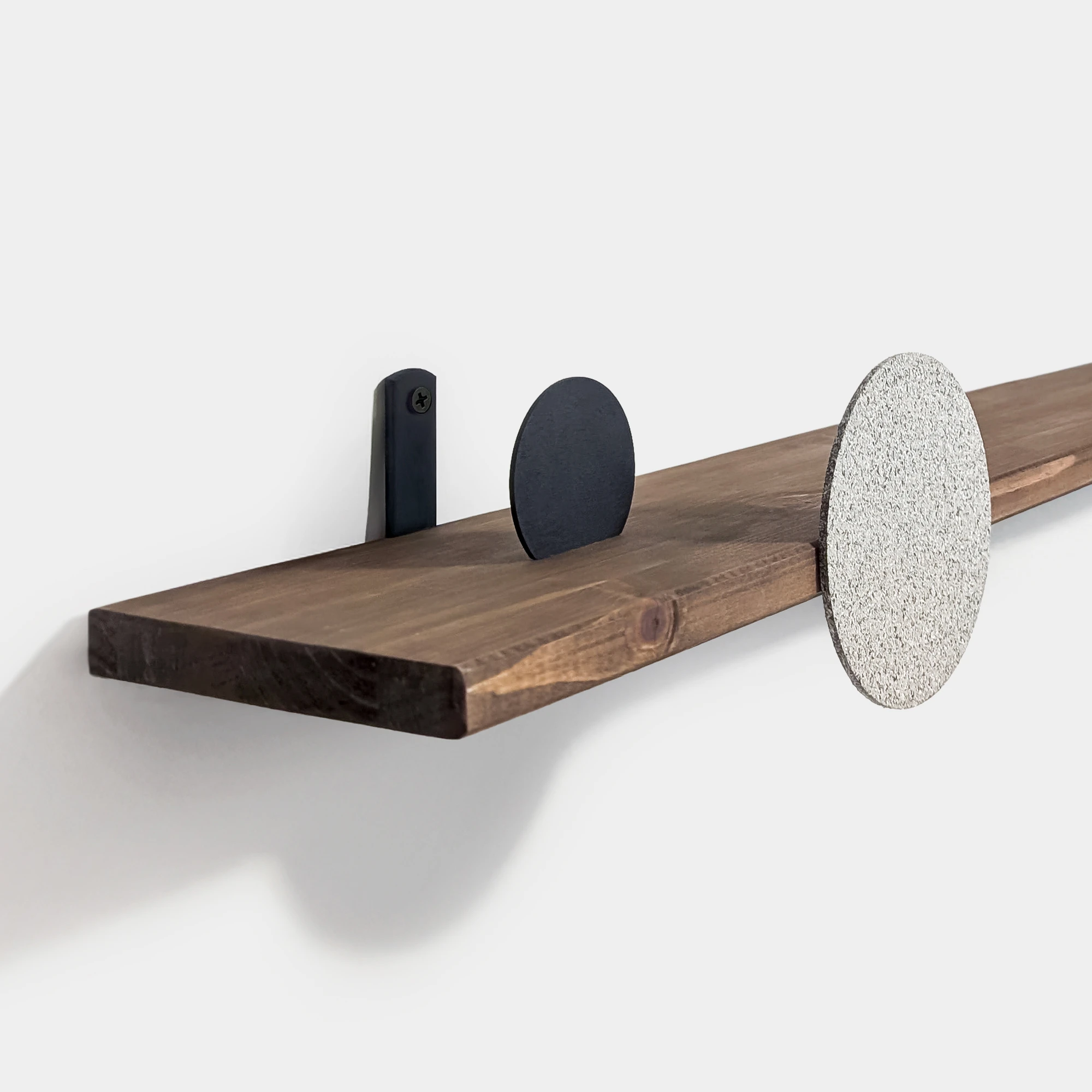 תקריב של מדף עץ עם מתלה חבוי ותוספת עיגולים דקורטיביים בצבע שחור וטקסטורת אבן