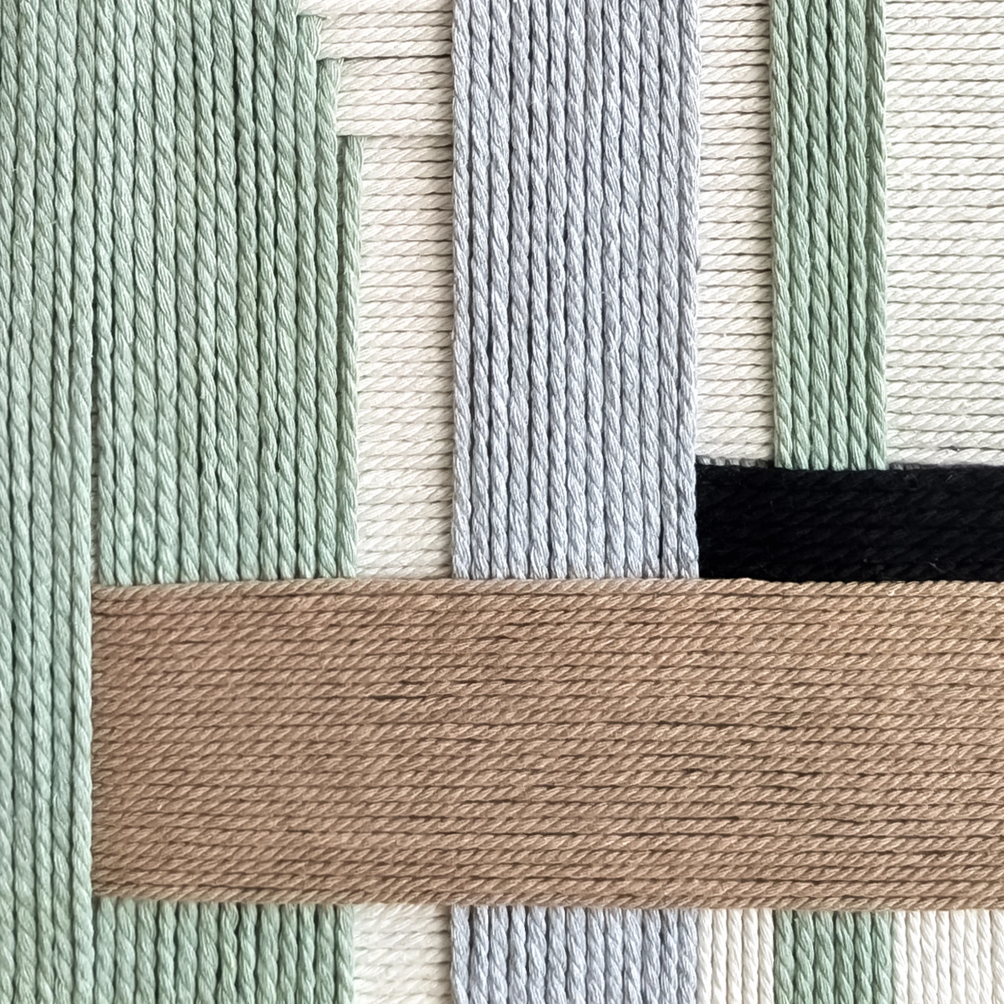 תקריב של אריגת חוטי כותנה בגווני שחור, אפור, חום, ירוק מרווה וגוון טבעי