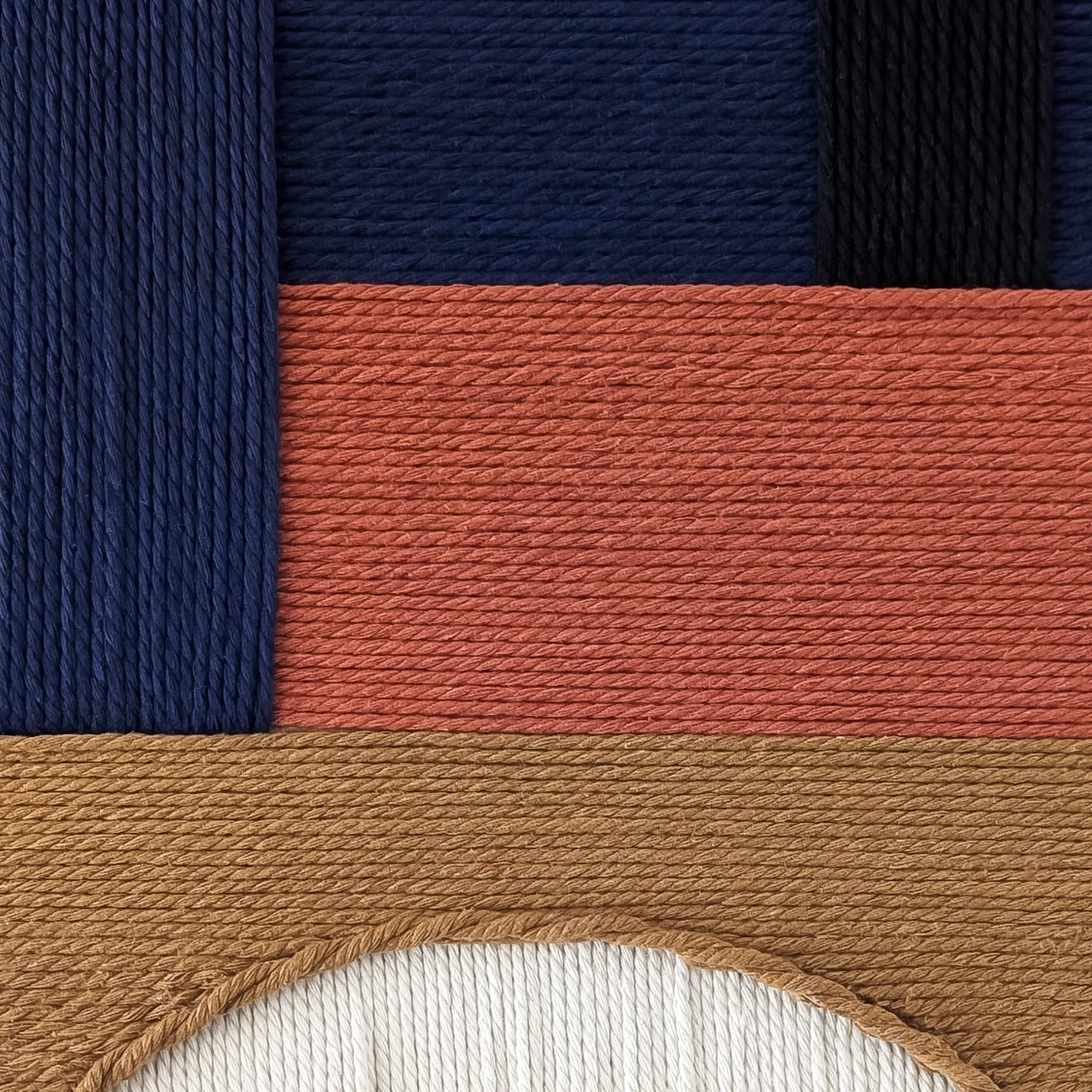 תקריב של אריגת חוטי כותנה בגווני שחור, כחול כהה, חמרה, חום וגוון טבעי
