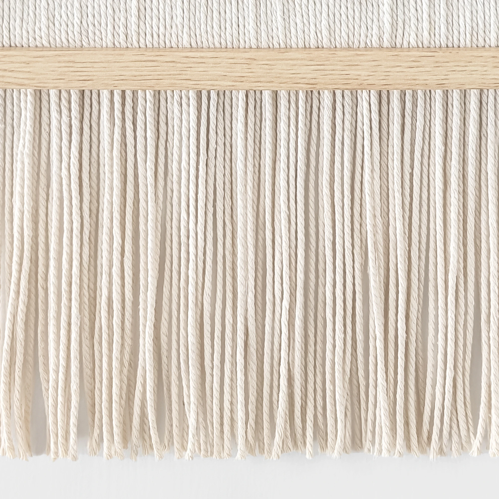תקריב של חוטי כותנה בגוון טבעי עוברים דרך מסגרת עץ