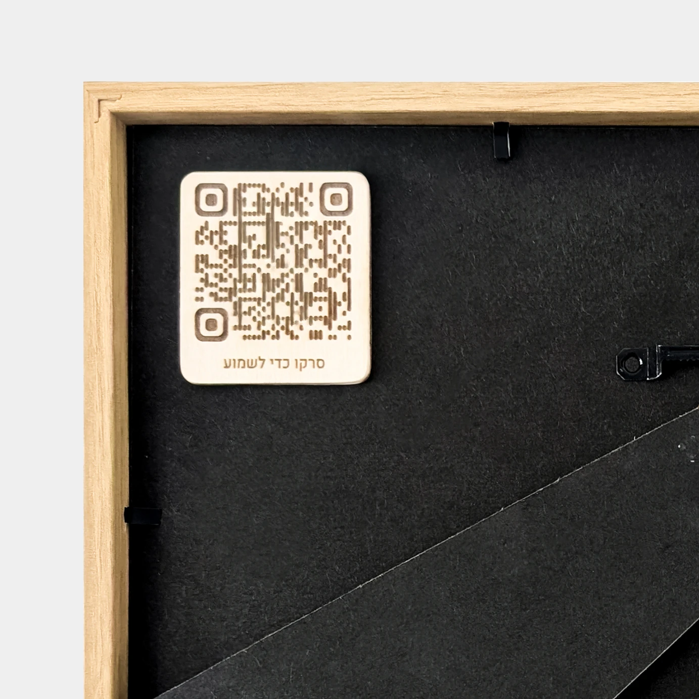 תקריב של קוד QR לסריקה לשמיעת הקלטה אישית, בחלק האחורי של מסגרת עץ